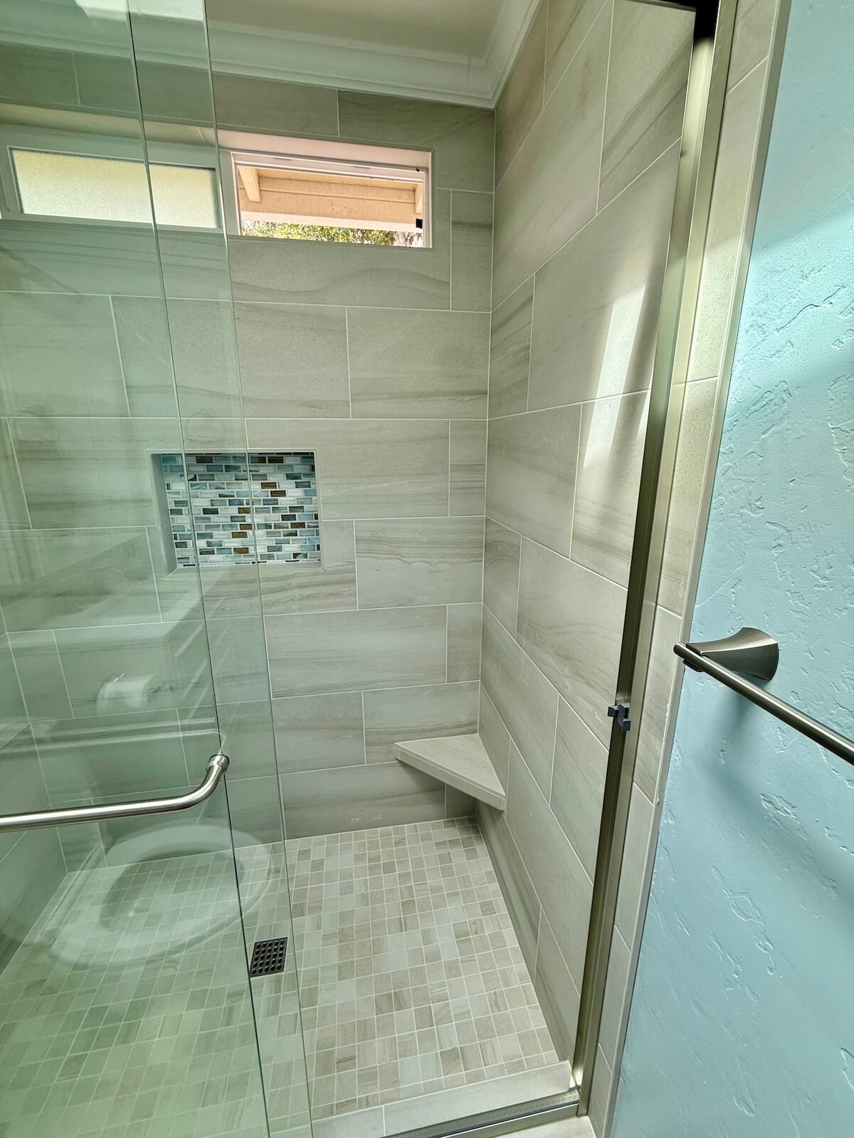 Tiled shower with mosaic accent niche and corner bench
