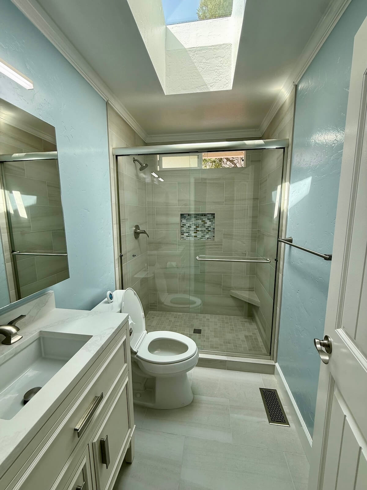 Remodeled bathroom with glass shower, toilet, and vanity under a skylight