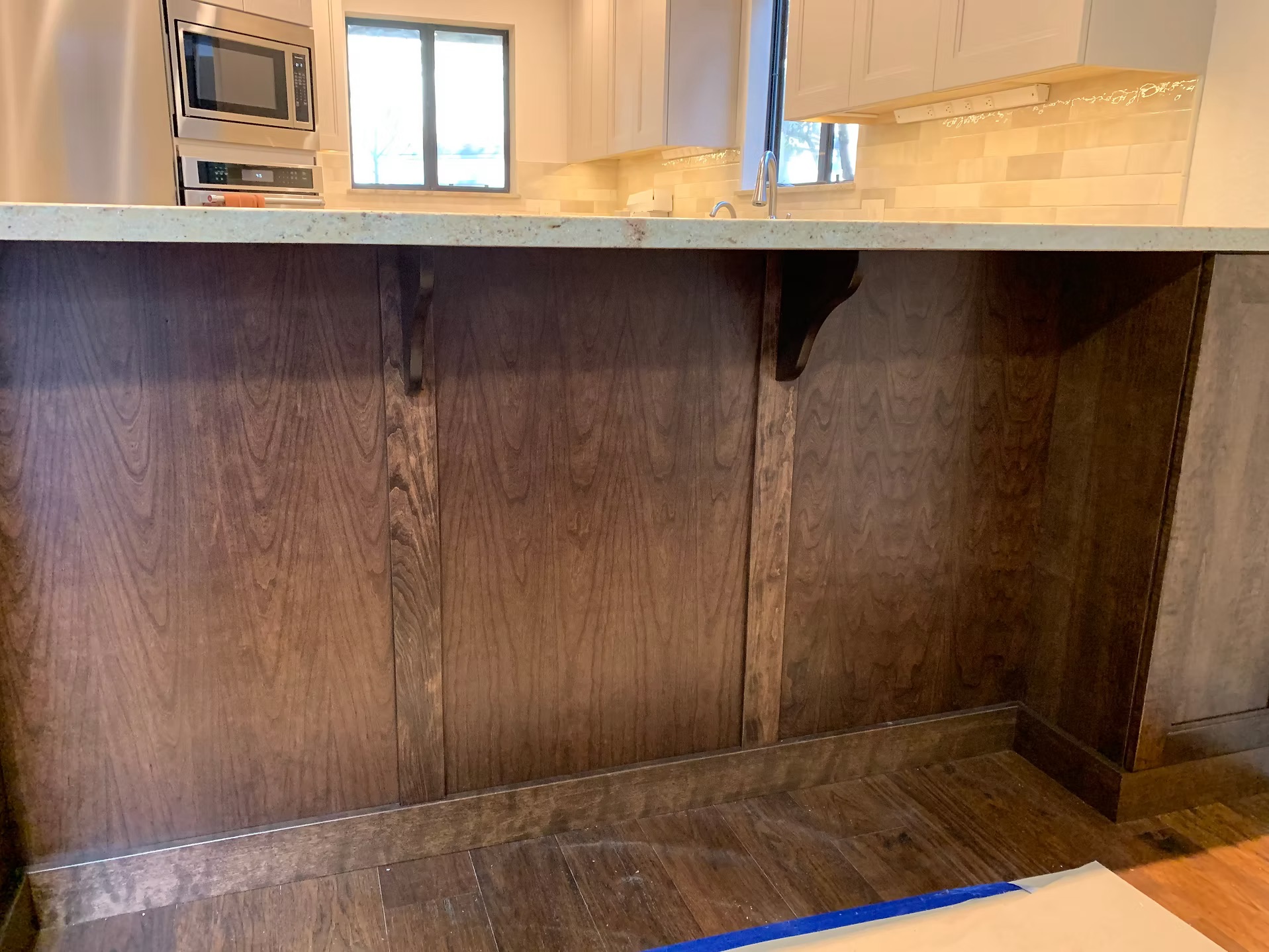 Close-up of stained wood island cabinetry and granite countertop overhang