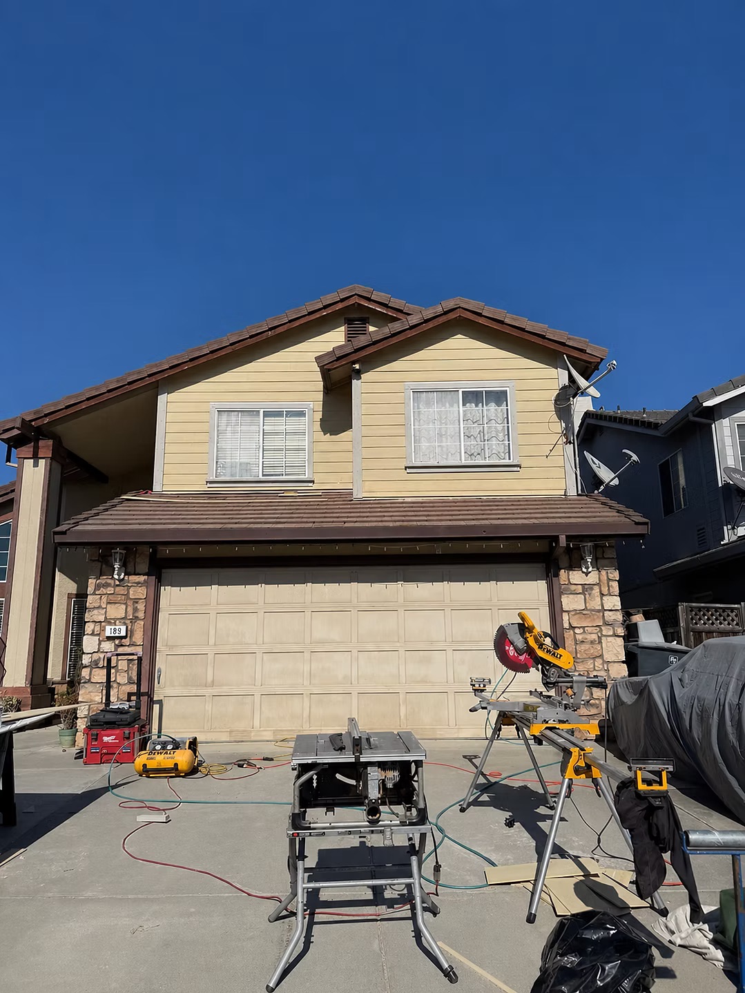Two-story home exterior with lap siding and stone accents, tools staged in driveway
