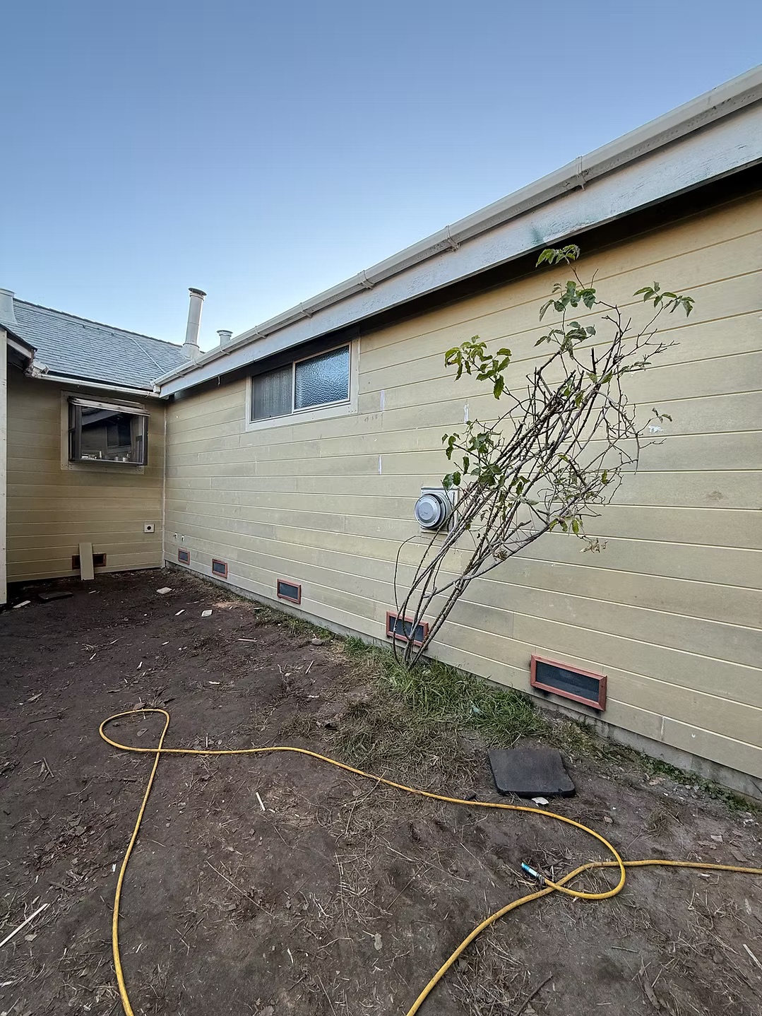 Tan lap siding with vent covers along the side of a home in evening light